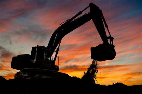 An excavator digging in silhouette against a sunset